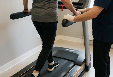 Physiothérapeute en gants corrigeant la posture d'un patient âgé sur un tapis roulant dans un centre de rééducation professionnel.