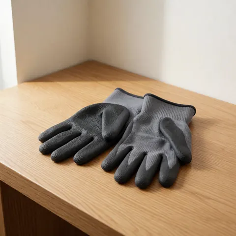 Gants de protection gris charbon sur une table en bois clair, avec texture antidérapante et renforts aux knuckles, éclairage naturel, pour réparation d'outils.