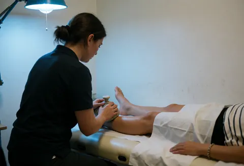 Physiothérapeute appliquant du gel froid sur la cheville d'un patient allongé sur une table de traitement dans un environnement clinique.