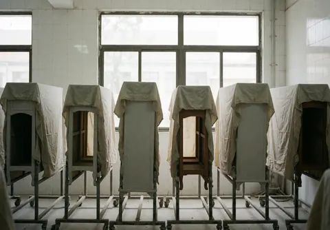 Des meubles restaurés recouverts d'un tissu protecteur dans une pièce de séchage avec grandes fenêtres et murs carrelés blancs.