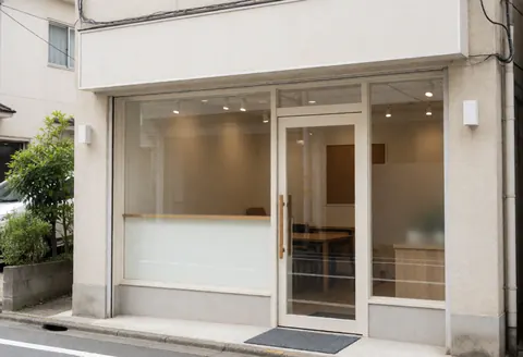 Vue de la façade extérieure d'un immeuble montrant l'entrée principale d'un bureau moderne équipée d'une grande porte en verre transparent et d'une fenêtre latérale.
