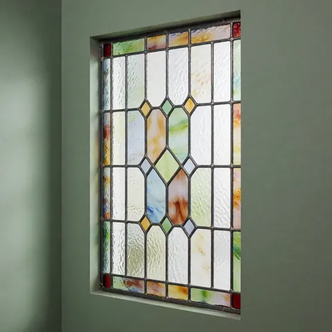 Vue rapprochée d'une fenêtre restaurée avec du verre décoratif, mettant en valeur le travail artisanal et les détails du design lumineux.