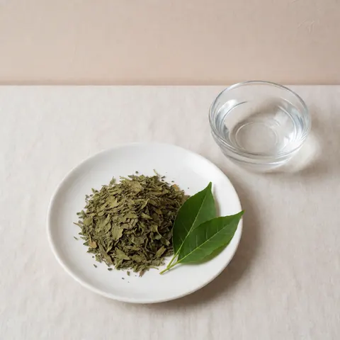 Assiette blanche contenant des feuilles de coca sèches et fraîches, accompagnée d'un verre d'eau, posée sur un tissu en lin clair avec un fond beige et une lumière douce.