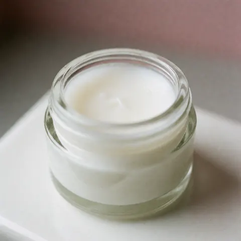 Baume kératolytique blanc dans un flacon en verre sur fond blanc, idéal pour la podologie et le soin des pieds et des mains.