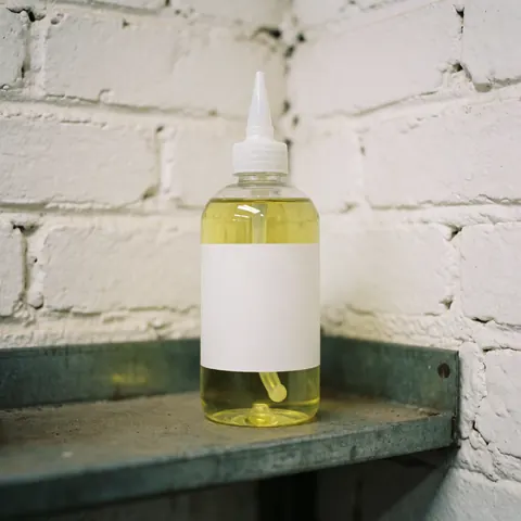 Bouteille transparente avec pipette blanche posée sur une étagère métallique devant un mur de briques blanches, produit de maintenance pour outils.