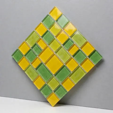 Panneau décoratif en mosaïque composé de pièces de verre jaune et vert disposées selon un motif géométrique, posé contre un mur gris neutre.