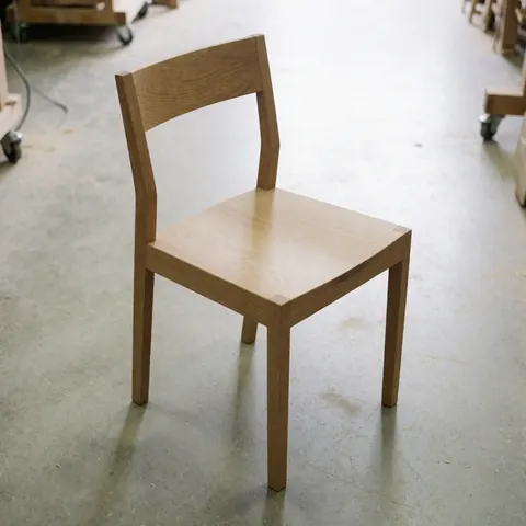 Vue de face d'une chaise style Shaker en bois massif restaurée, montrant les détails du travail de menuiserie et la finition naturelle sur fond neutre.