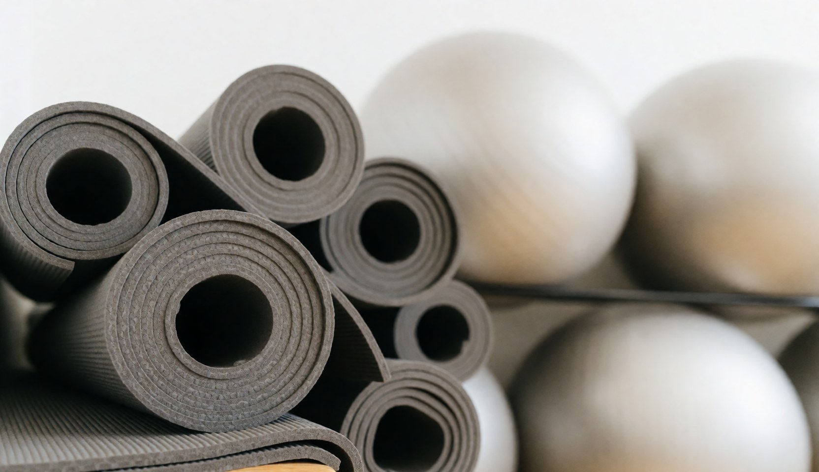 Fond neutre et épuré d'une zone de gymnastique, présentant des tapis de yoga et des ballons de stabilité sur un sol clair, idéal pour un arrière-plan professionnel.