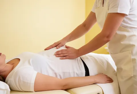 Une thérapeute maternelle réalise un massage avec des huiles essentielles sur le dos d'une cliente enceinte dans un cadre calme et professionnel.