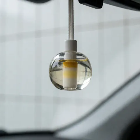 Gros plan sur un diffuseur d'arôme automobile transparent en forme de perle, posé sur une surface blanche, laissant voir la lumière naturelle à travers son design minimaliste.