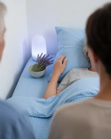 Une personne se repose dans un lit avec de la lavande et un diffuseur, profitant de l'aromathérapie dans une chambre aux draps bleus et à la lumière douce.