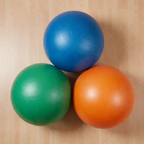 Plusieurs boules suisses colorées disposées sur un sol clair dans un environnement minimaliste, utilisées pour la rééducation et le renforcement musculaire en cabinet de kinésithérapie.