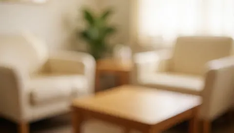 Intérieur d'une salle d'attente d'ostéopathie avec canapés beige, table en bois et plante verte, éclairage chaleureux pour un fond neutre.