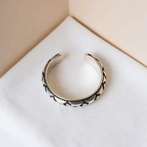 Bracelet en argent avec finition oxydé, détails artisanaux visibles, sur tissu blanc, mur beige, éclairage doux, produit de joaillerie.