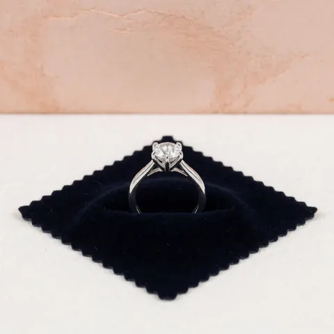Détail macro d'une griffe de bague en métal argenté, solidifiée pour sécuriser un diamant. La pièce est posée sur un fond sombre texturé, mettant en valeur la précision du travail artisanal et la qualité du bijou.