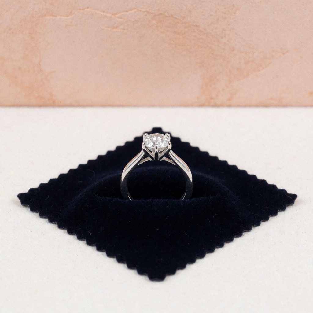 Détail macro d'une griffe de bague en métal argenté, solidifiée pour sécuriser un diamant. La pièce est posée sur un fond sombre texturé, mettant en valeur la précision du travail artisanal et la qualité du bijou.