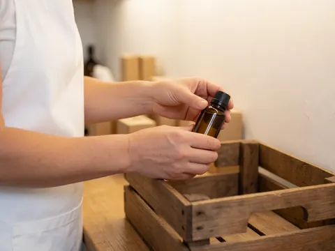 Prise de vue rapprochée des mains d'une femme emballant soigneusement des bouteilles d'huile essentielle dans une boîte en bois sur un bureau.