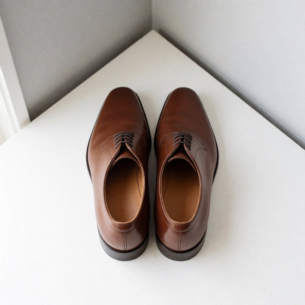 Paire de chaussures de ville en cuir marron restaurée, présentée sur un fond blanc avec une lumière naturelle mettant en valeur la qualité du travail.