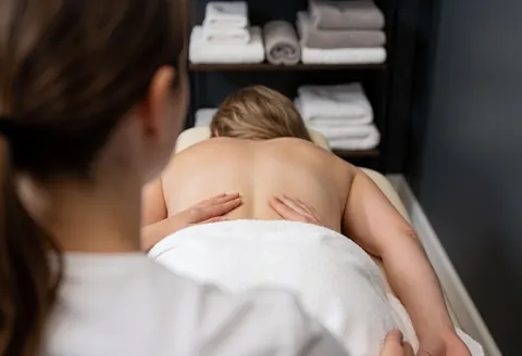 Un thérapeute réalise un massage chiropratique sur le dos d'un patient allongé sur une table, avec des serviettes en arrière-plan dans un cadre clinique et relaxant.