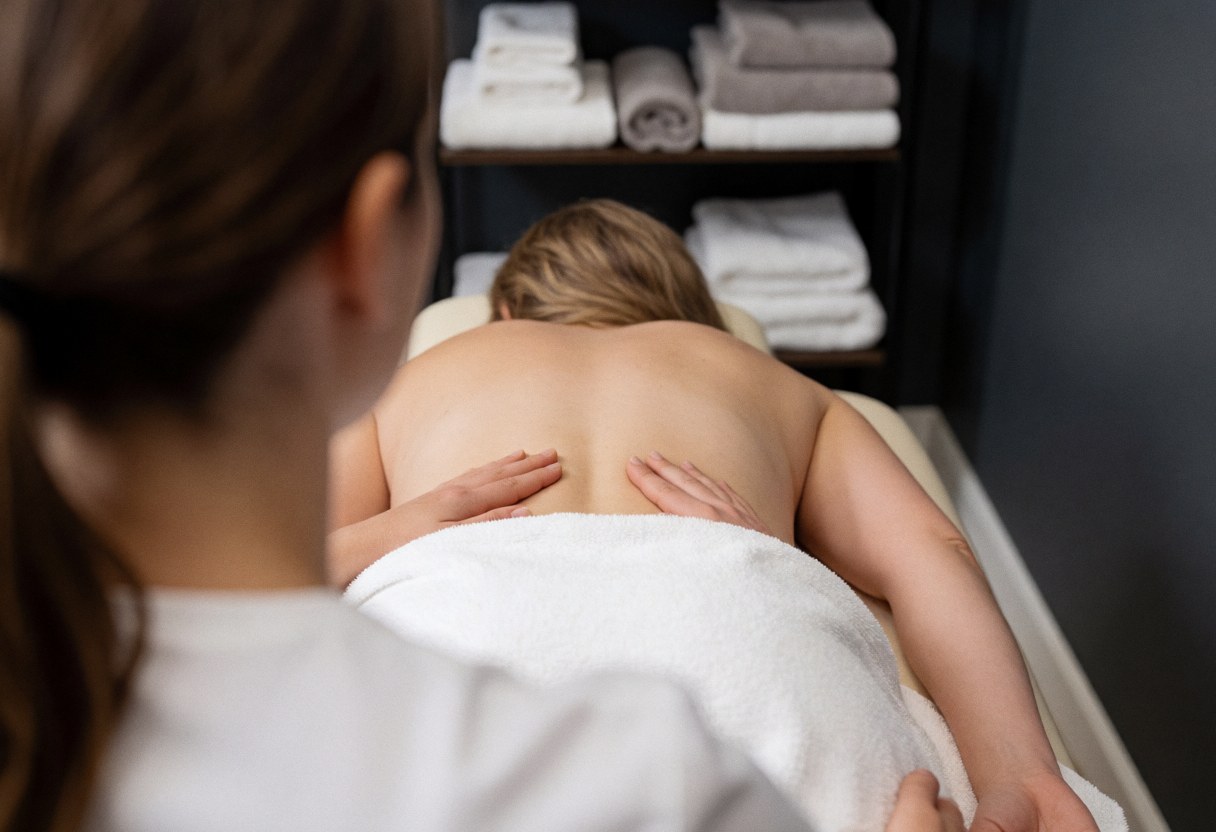 Un thérapeute réalise un massage chiropratique sur le dos d'un patient allongé sur une table, avec des serviettes en arrière-plan dans un cadre clinique et relaxant.