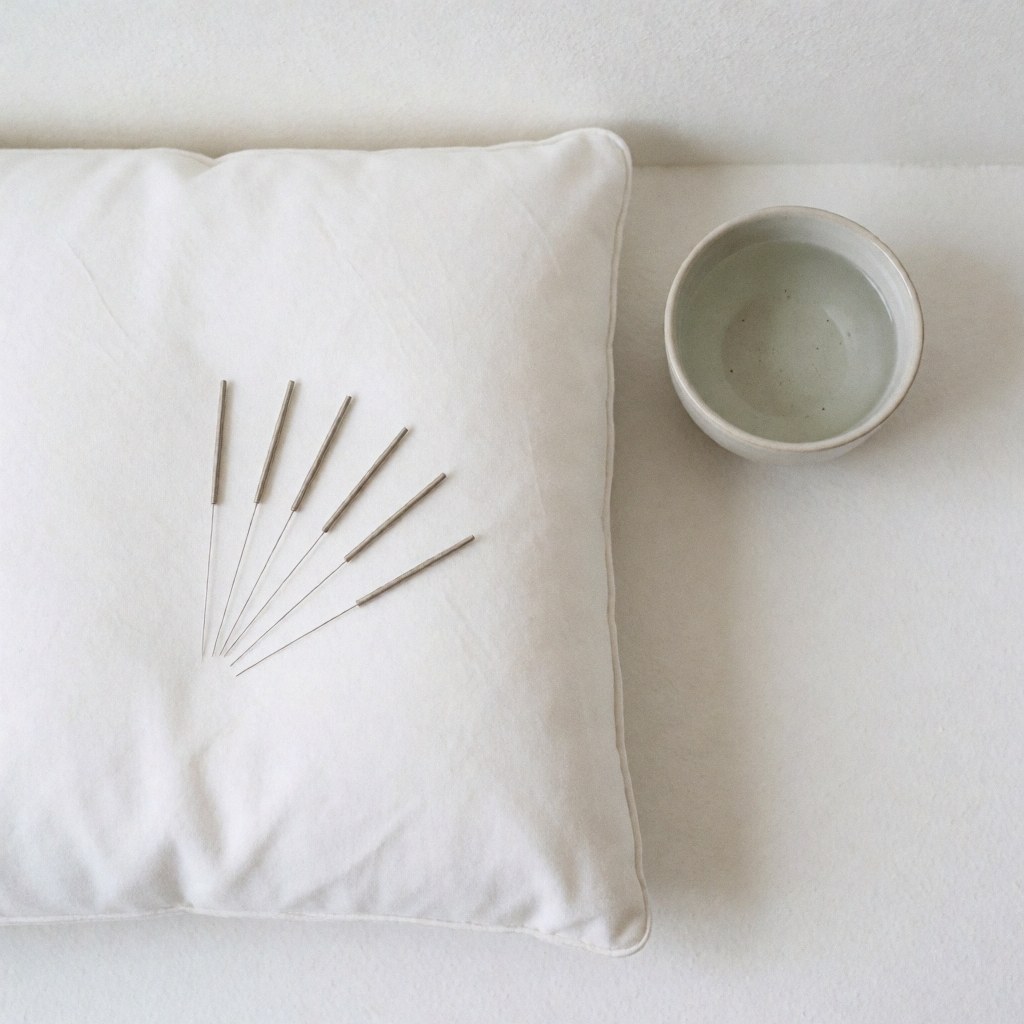 Aiguilles d'acupuncture disposées proprement sur un fond blanc minimaliste, accompagnées d'un coussin et d'une tasse d'eau pour le bien-être.