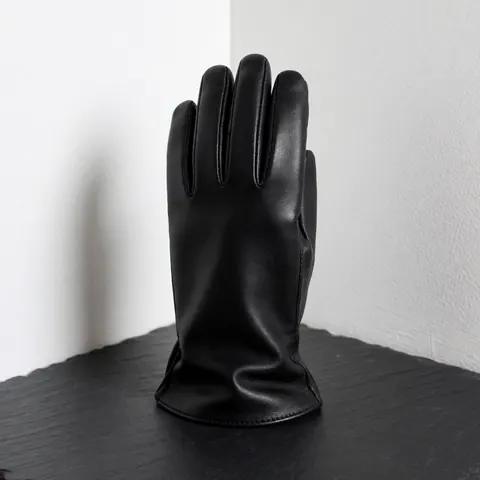 Gant en cuir noir élégant et de qualité posé sur une surface d'ardoise sombre, avec un fond blanc et une lumière douce mettant en valeur la texture.