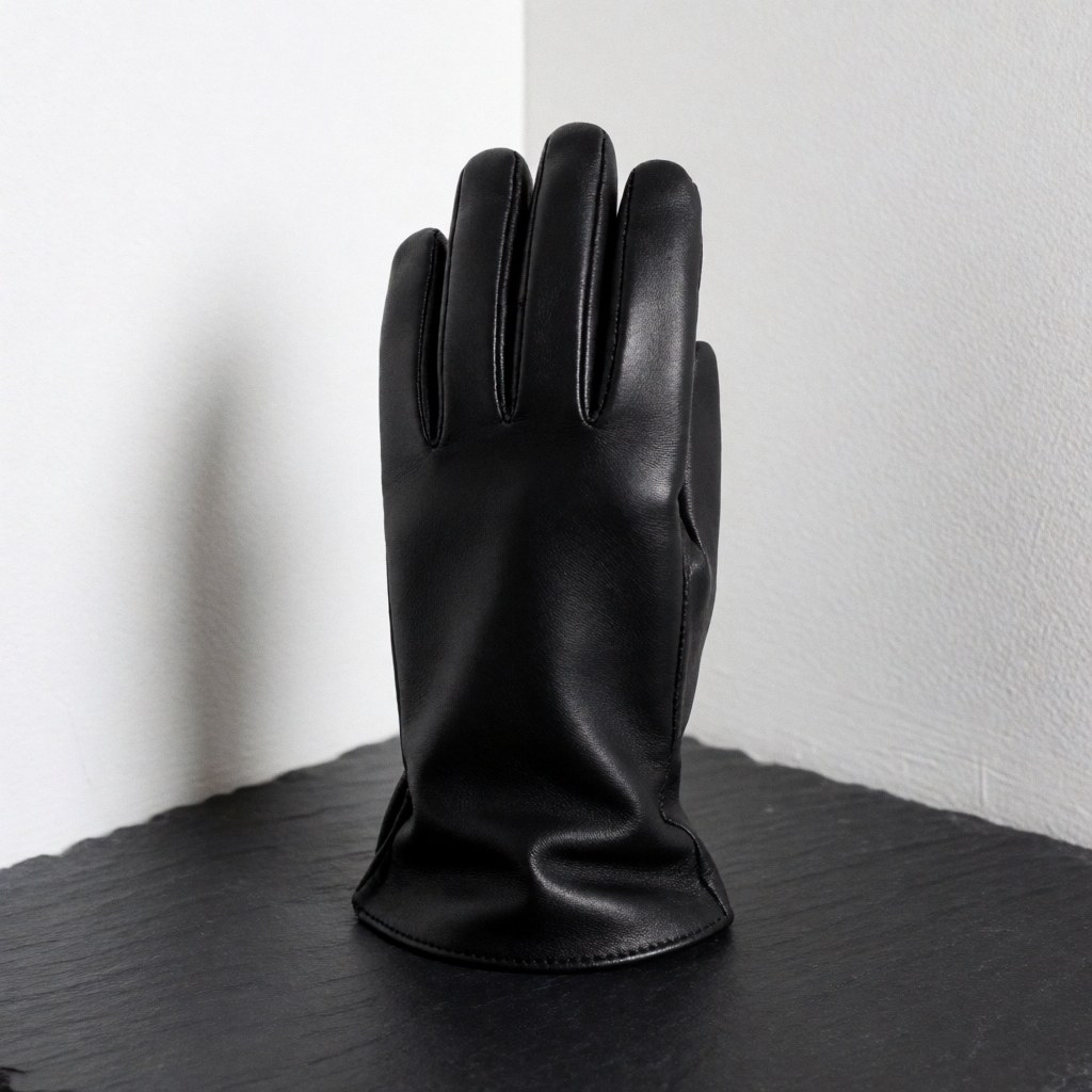 Gant en cuir noir élégant et de qualité posé sur une surface d'ardoise sombre, avec un fond blanc et une lumière douce mettant en valeur la texture.