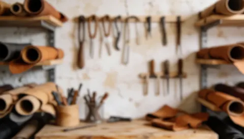 Arrière-plan flou d'un atelier de cuir montrant des rouleaux de peau, des outils suspendus et une table de travail, idéal pour du texte commercial.