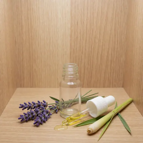 Bouteille en verre contenant de l'huile essentielle avec pipette, disposée sur une surface en bois avec des fleurs de lavande et un citron vert pour l'aromathérapie.