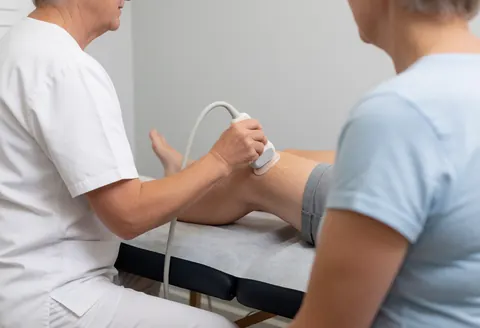 Un thérapeute applique un traitement par ultrasons sur le genou d'une patiente assise dans un cabinet de kinésithérapie professionnel.