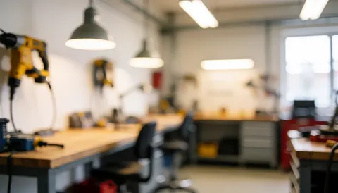 Arrière-plan flou d'un atelier de réparation montrant des outils, une table en bois, une chaise et un éclairage chaud, idéal pour présenter des services techniques.