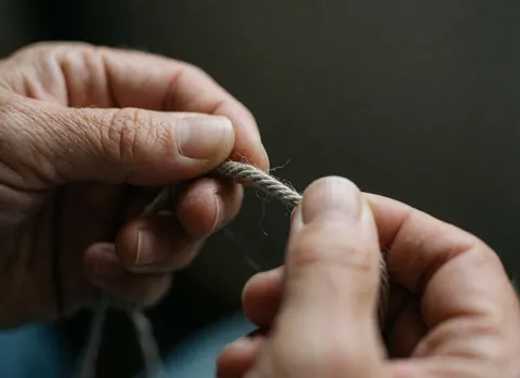 Gros plan d'une fibre de fil de lin ciré sur un fond sombre, mettant en valeur la texture et les détails du matériau utilisé par un artisan.