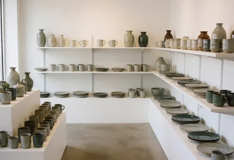 Intérieur minimaliste d'une boutique vide présentant des étagères en béton et une vaisselle artisanale sous un éclairage naturel.