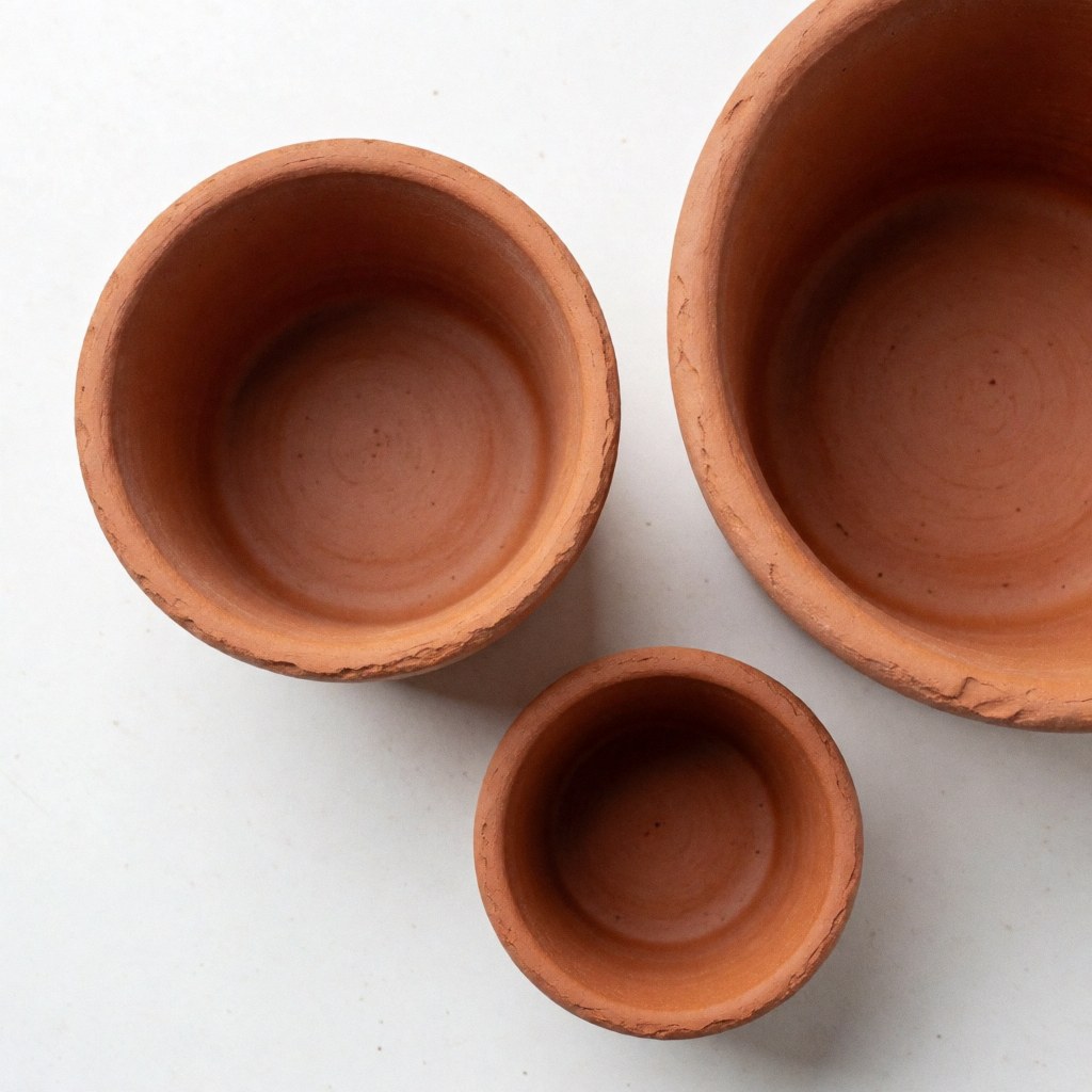 Plusieurs pots de fleurs en terre cuite non émaillée disposés sur une surface blanche, mettant en valeur leur texture naturelle et artisanale.