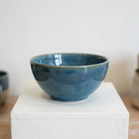 Bol en céramique artisanale de couleur bleue brillante posé sur un support blanc dans un studio éclairé pour la présentation d'un produit.