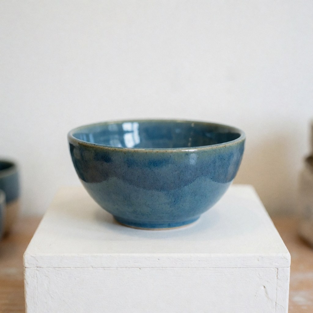 Bol en céramique artisanale de couleur bleue brillante posé sur un support blanc dans un studio éclairé pour la présentation d'un produit.