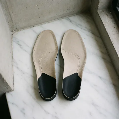 Présentation de semelles anatomiques surélevées avec un design ergonomique et minimaliste, disposées sur une surface texturée claire pour mettre en valeur leur forme.