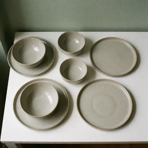 Ensemble de vaisselle en céramique artisanale aux tons neutres et naturels, incluant assiettes et bols au design épuré et moderne.
