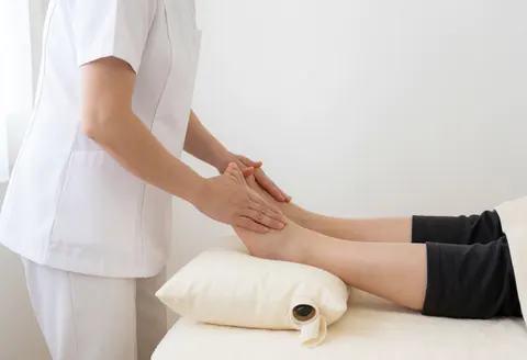 Un praticien en uniforme blanc applique une technique de réflexologie sur le pied d'un client allongé sur une table de massage avec une housse blanche.
