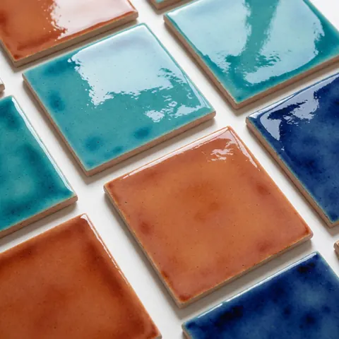Des carreaux de céramique artisanaux aux couleurs vives turquoise, terracotta et bleu disposés sur une surface blanche avec des touches de bois naturel.
