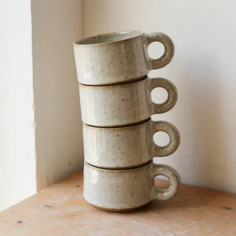 Plusieurs tasses en céramique artisanale sont empilées les unes sur les autres, présentant une finition mate et des tons neutres.