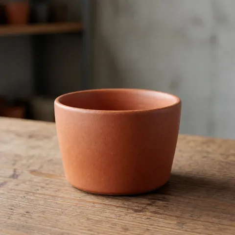 Tasse de café artisanale en terre cuite posée sur une table en bois, mettant en valeur sa texture naturelle et son design fait main.