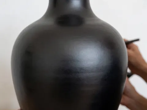 Vase en argile noire polie avec finition brillante sur fond blanc, mettant en valeur la texture lisse et le travail artisanal de la céramique.