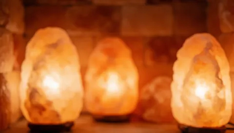 Lampe en pierre de sel émettant une lueur orange douce sur fond sombre, créant une ambiance relaxante et chaleureuse pour un spa ou un massage.