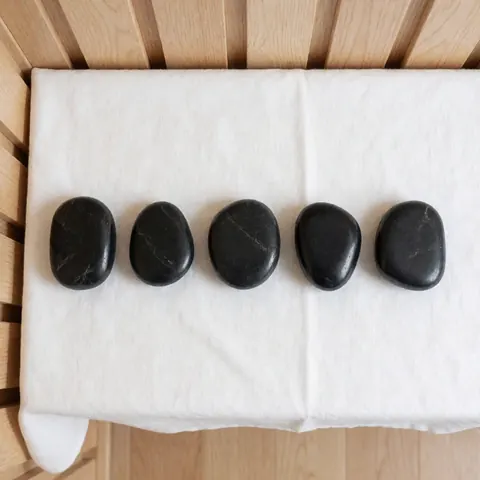 Cinq pierres noires lisses et brillantes posées sur un tissu blanc, sur un fond en bois clair, évoquant le bien-être et les soins spa.