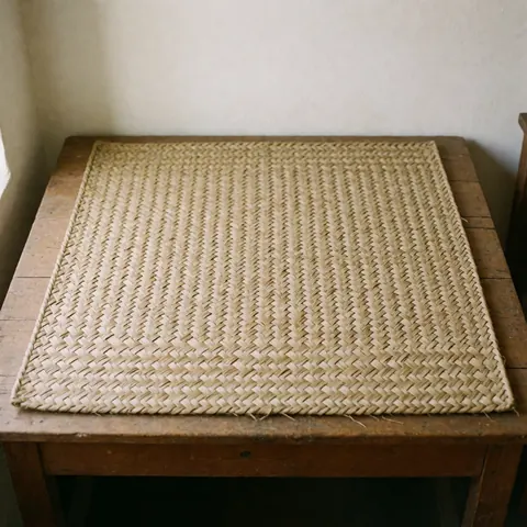Un tapis artisanal tissé en fibres naturelles de palmier est posé à plat sur une surface en bois clair, mettant en valeur sa texture rustique et ses tons neutres.