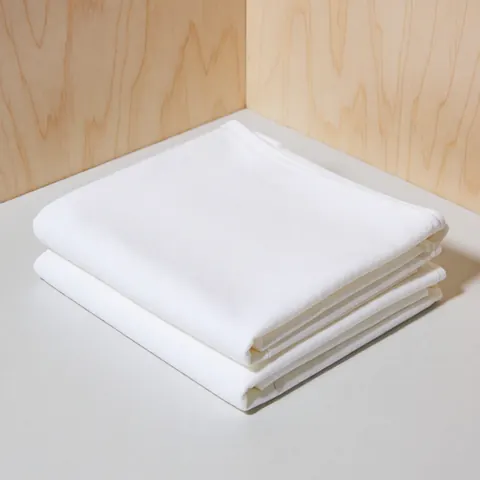 Un tissu en coton blanc et doux posé sur une surface en bois, offrant une texture pure et minimaliste pour la décoration intérieure.