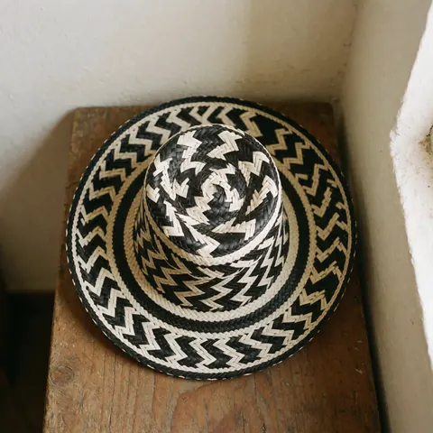 Un chapeau vueltiao traditionnel colombien, noir et blanc, posé sur une surface en bois rustique avec un éclairage naturel.