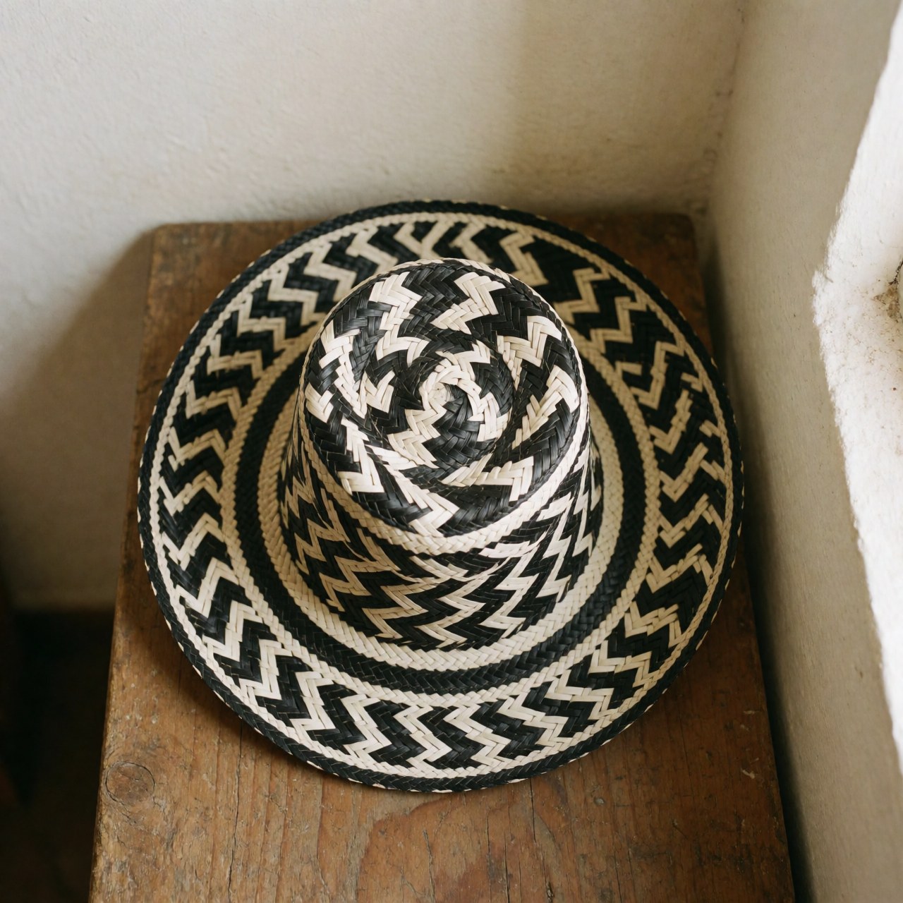 Un chapeau vueltiao traditionnel colombien, noir et blanc, posé sur une surface en bois rustique avec un éclairage naturel.
