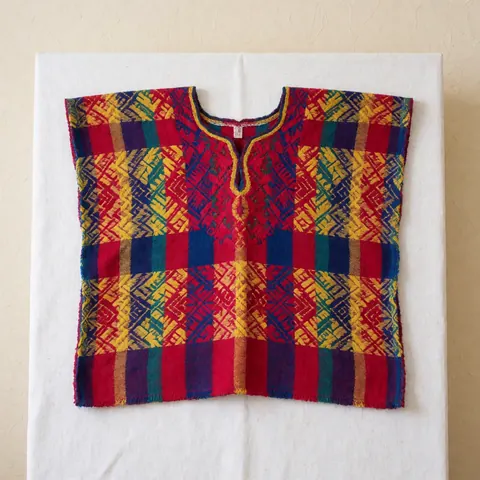 Huipil traditionnel guatémaltèque aux motifs géométriques colorés, présenté sur un fond blanc uni pour une utilisation commerciale.